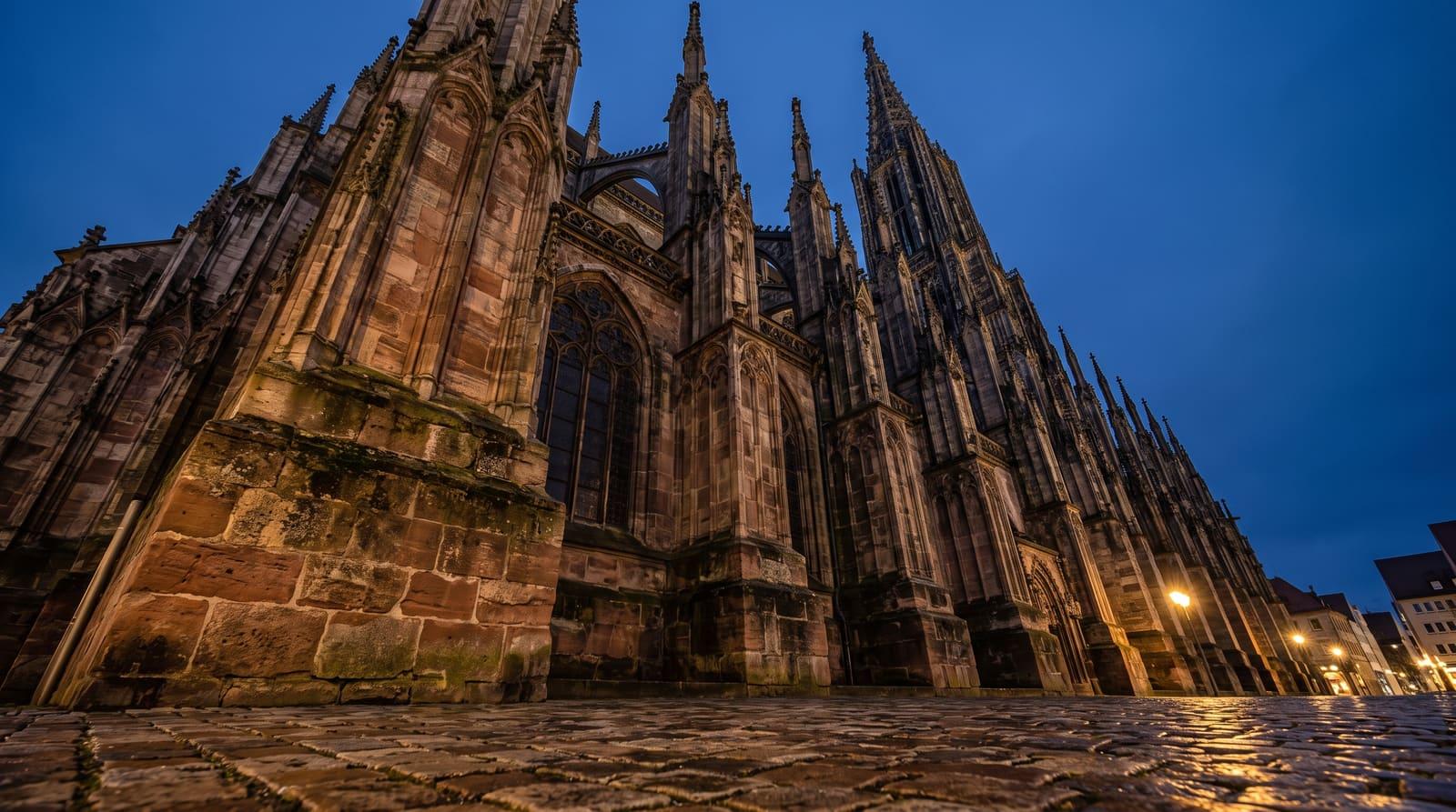 Massive Strebepfeiler und Sandsteinquader am Sockel des Ulmer Münsters in der blauen Stunde als Sinnbild für das Fundament vor dem ersten Immobilienkauf